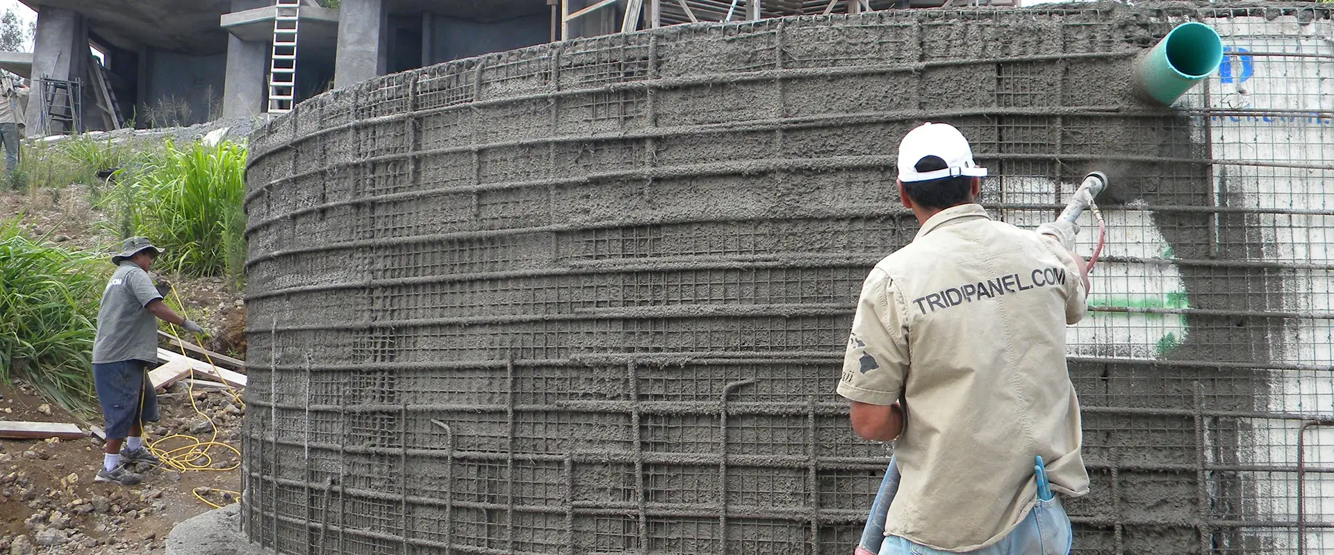Man spraying concrete onto a wire mesh wall.