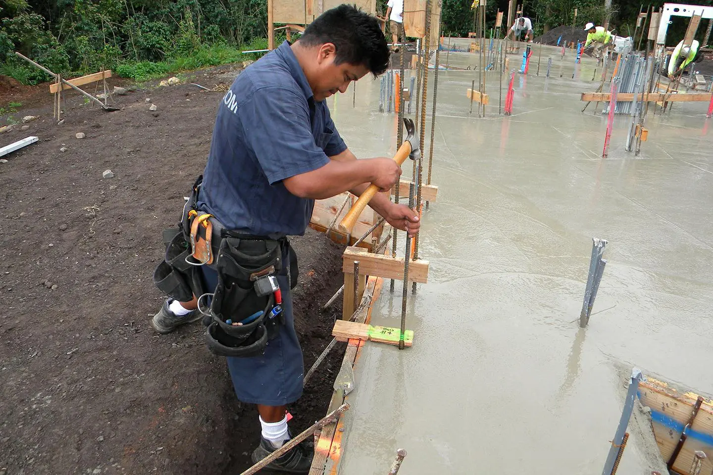 Construction worker hammering rebar in wet concrete.