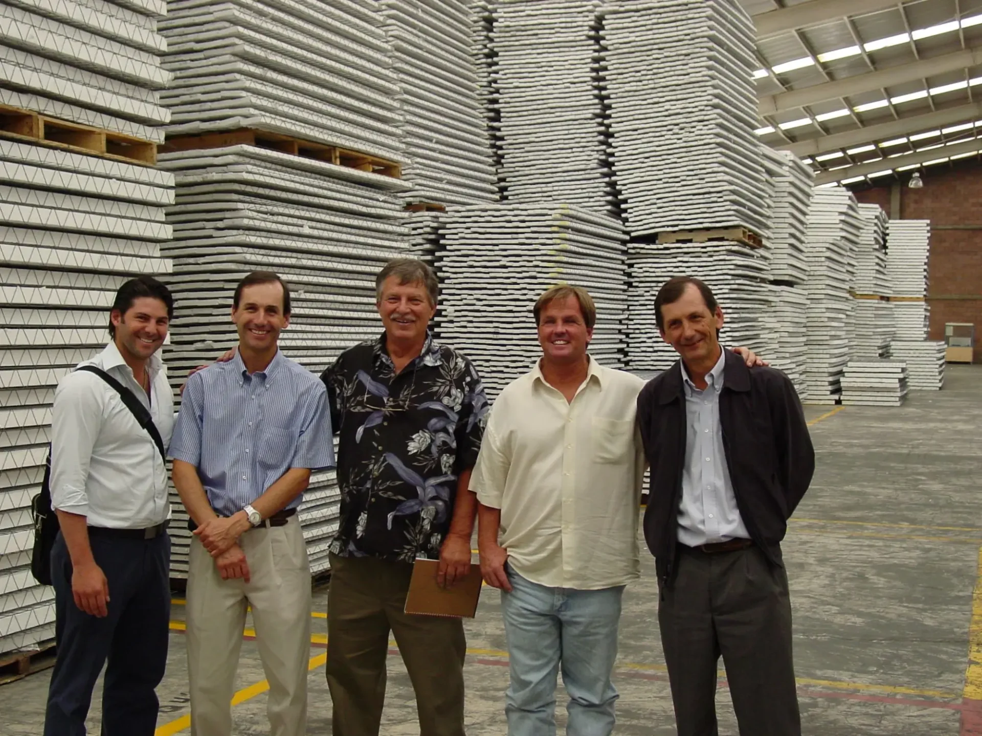 Five men in a warehouse with stacked materials.