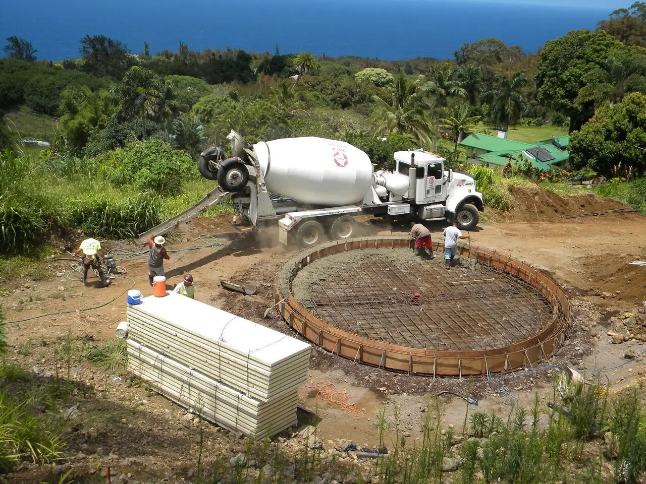 Concrete truck pouring foundation on hillside.